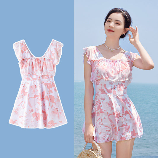 Women's pink and white floral one-piece swimsuit with ruffled cap sleeves and a skirted bottom, shown on a model by the ocean. - Image 2
