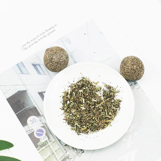 A hand holds a spherical catnip ball made of dried mint leaves and stems, light green and brown in color. - Image 2