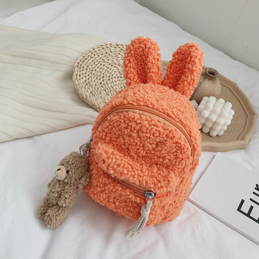 Pink fuzzy mini backpack with bear ears and a small white teddy bear keychain on a white bed. - Image 2