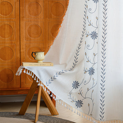 White semi-sheer curtain with brown botanical embroidery and white tassels, draped over a small wooden table. - Image 8