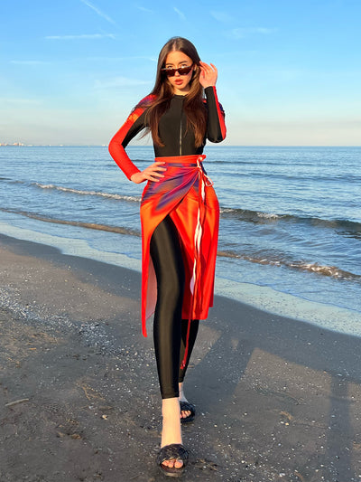 Woman in a black long-sleeve rash guard, black swim leggings, and a vibrant tie-dye sarong on a sunny beach. - Image 9