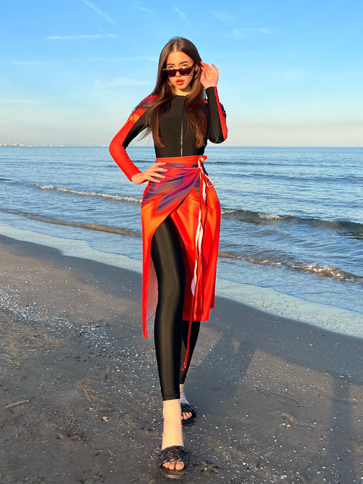 Woman in a black long-sleeve rash guard, black swim leggings, and a vibrant tie-dye sarong on a sunny beach. - Image 9