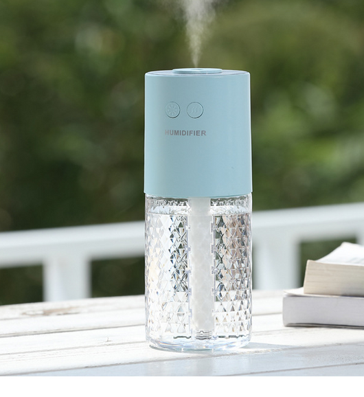 Dark blue and clear portable humidifier with a textured water tank on a white desk next to a laptop.