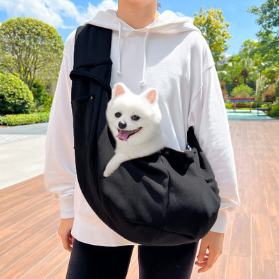 Person in white hoodie carrying a happy white dog in a navy blue pet sling bag outdoors. - Image 28