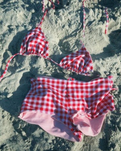 Red and white gingham high-waisted bikini set with triangle top, laid on sand under sunlight. - Image 6