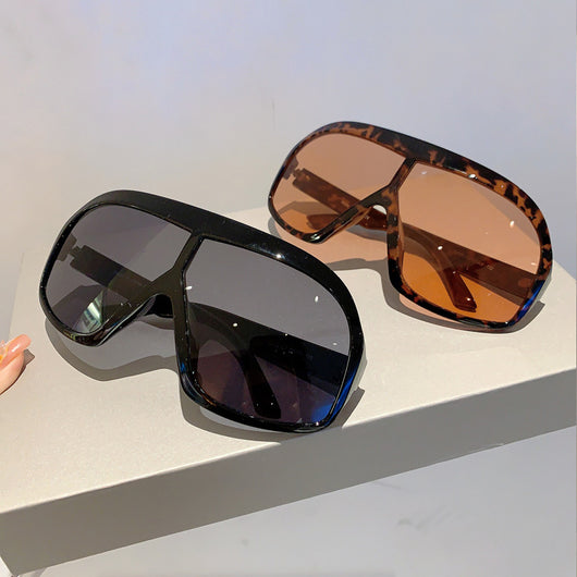 Oversized women's shield sunglasses with a tortoiseshell frame and brown-tinted lenses, held by a hand. - Image 17
