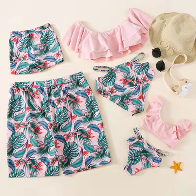 Family matching swimsuits with pink tropical floral and leaf print. Includes women's ruffled bikini, girl's one-piece, and men's/boy's swim shorts. - Image 3