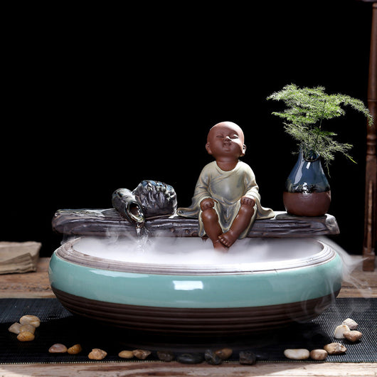 Ceramic flowing water ornament with a meditating monk figurine, small plant, and misting humidifier in a teal and brown bowl. - Image 15