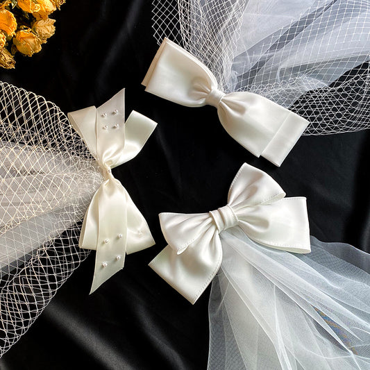 White birdcage veil with a cream satin bow and faux pearls, attached to a woven straw base, 80cm yarn length.