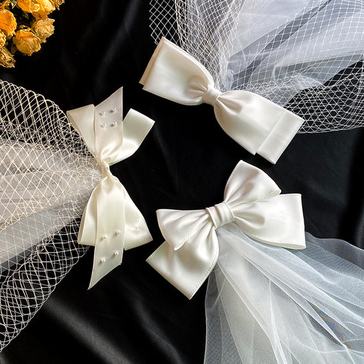 White birdcage veil with a cream satin bow and faux pearls, attached to a woven straw base, 80cm yarn length.