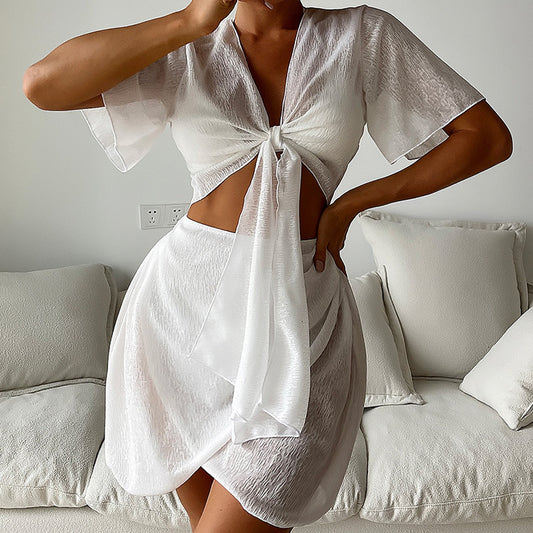 White two-piece swimwear set with a tie-front crop top and a high-waisted skirt with an asymmetrical ruffled hem.