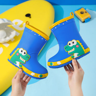 Bright yellow children's rain boots with a green cartoon dinosaur design and orange trim, held by hands. - Image 8