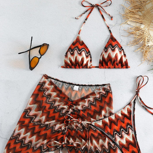 Three-piece printed swimsuit with a red and teal abstract pattern, featuring a halter bikini top, bottom, and mesh wrap skirt with drawstring.