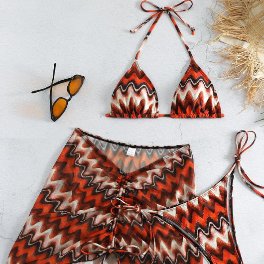 Three-piece printed swimsuit with a red and teal abstract pattern, featuring a halter bikini top, bottom, and mesh wrap skirt with drawstring.