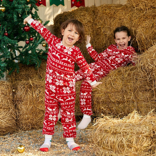 Family of four wearing matching red and white Christmas pajamas with reindeer and snowflake patterns, smiling. - Image 6
