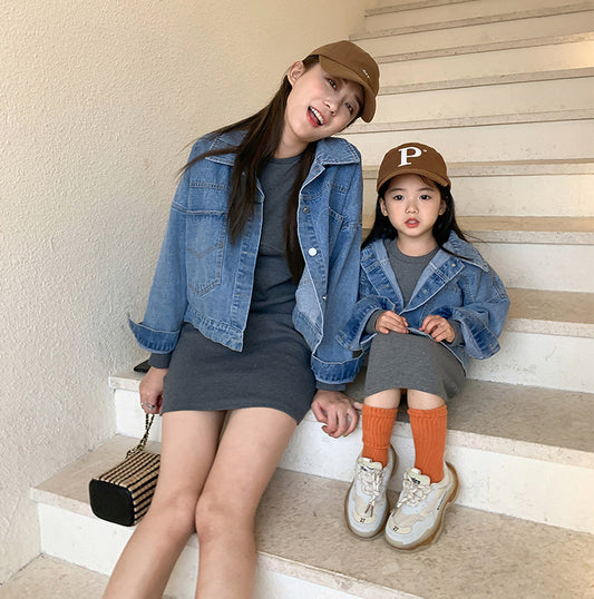 Woman and child in matching outfits: light blue denim jackets and dark gray knitted mini dresses, with baseball caps and sneakers.