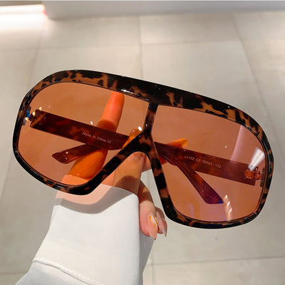 Oversized women's shield sunglasses with a tortoiseshell frame and brown-tinted lenses, held by a hand. - Image 3