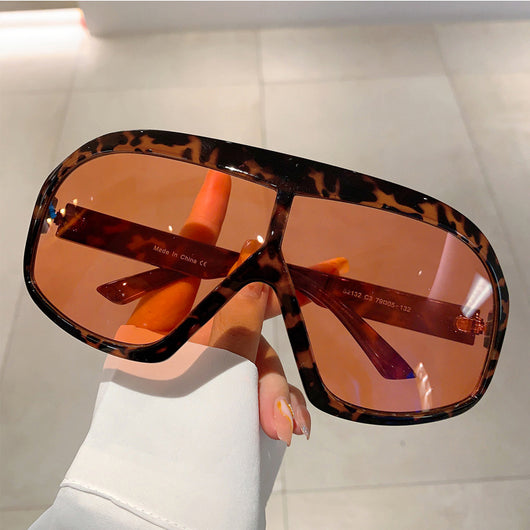 Oversized women's shield sunglasses with a tortoiseshell frame and brown-tinted lenses, held by a hand. - Image 3
