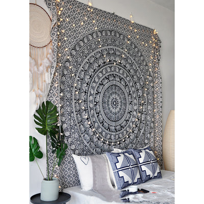 Black and white mandala tapestry with string lights hanging above a bed with blue and white patterned pillows. - Image 7