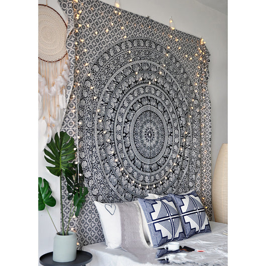 Black and white mandala tapestry with string lights hanging above a bed with blue and white patterned pillows. - Image 7