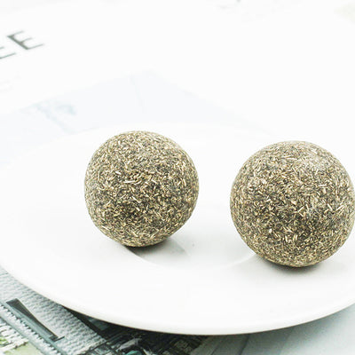 A hand holds a spherical catnip ball made of dried mint leaves and stems, light green and brown in color. - Image 9