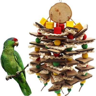 Parrot gnawing toy made of stacked cardboard, corn husks, and colorful wooden beads, with a parrot perched nearby.