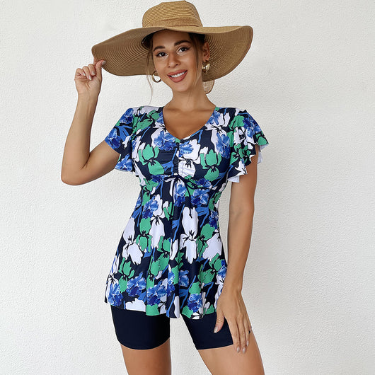Woman in a blue, black, and white floral print swim top with flutter sleeves and black swim shorts. - Image 4