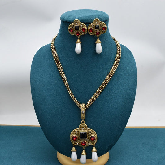 Vintage gold-toned necklace with double chain, ornate pendant featuring red and black glass inlays, and three white pearl tassels.