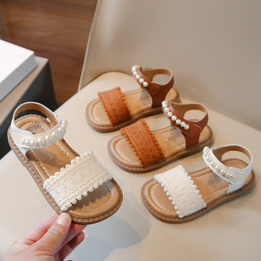 Children's white sandals with pearl ankle straps, woven front strap, and brown sole, featuring a Velcro closure.