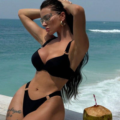 Woman in a black pure color bikini with gold O-rings, featuring a push-up top and high-cut bottoms, by the ocean.