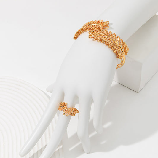Gold wheat ear leaf cuff bracelet and matching open ring set on a white textured surface.