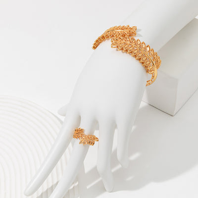 Gold wheat ear leaf cuff bracelet and matching open ring set on a white textured surface.
