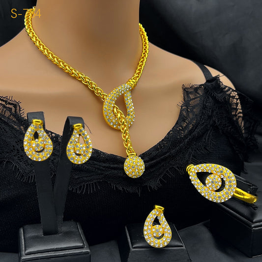 Gold-plated four-piece jewelry set with teardrop rhinestone necklace, bracelet, earrings, and ring on red velvet stands.