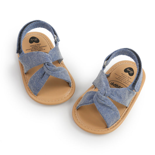 Black baby sandals with knotted cross straps and a matching black floral headband on a white background. - Image 29