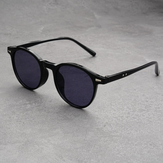 Fashionable round-frame sunglasses with transparent gray frames and dark gray lenses on a gray surface.
