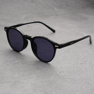 Fashionable round-frame sunglasses with transparent gray frames and dark gray lenses on a gray surface.