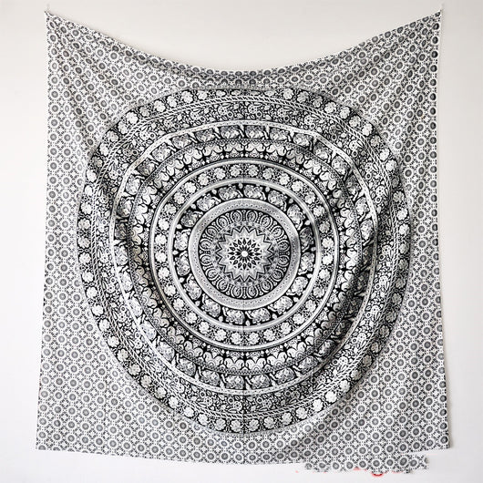 Black and white mandala tapestry with string lights hanging above a bed with blue and white patterned pillows.