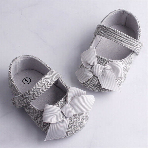 Grey herringbone baby crib shoes with white grosgrain bows and a single strap, perfect for toddlers.