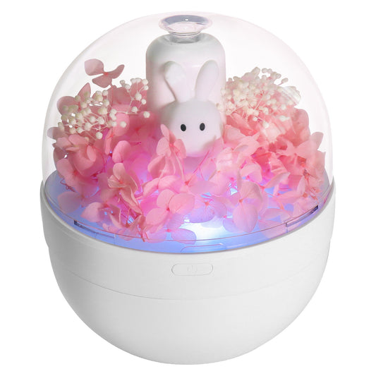 White rabbit preserved flower aromatherapy humidifier with pink flowers and blue light under a clear dome.