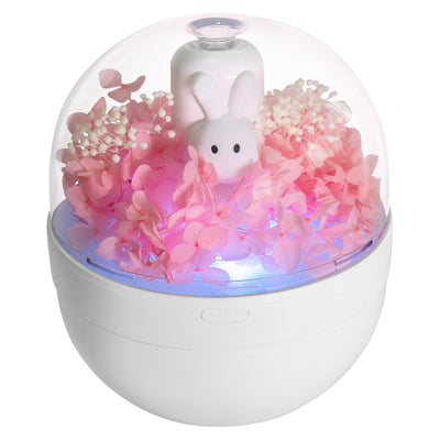 White rabbit preserved flower aromatherapy humidifier with pink flowers and blue light under a clear dome.