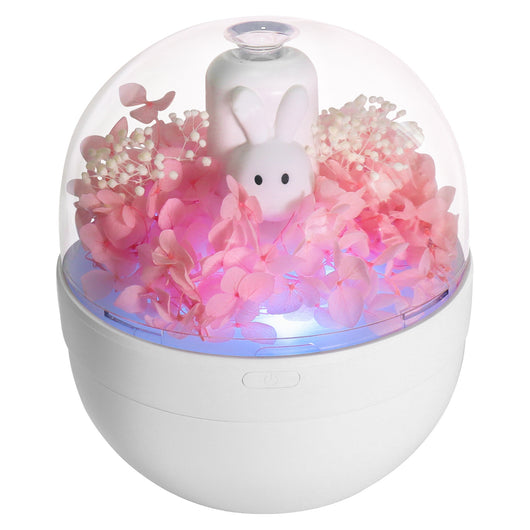 White rabbit preserved flower aromatherapy humidifier with pink flowers and blue light under a clear dome.