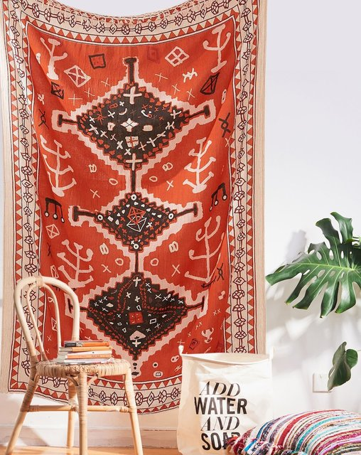 Red tapestry with black and white geometric tribal pattern hanging on a white wall above decorative pillows. - Image 7