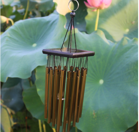 Bronze wind chime with multiple metal tubes hanging from a dark rectangular top, set against green lotus leaves. - Image 4