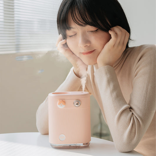 White cylindrical humidifier with ribbed texture, clear base, brown bear button, and silver dial, emitting mist on a white table. - Image 7
