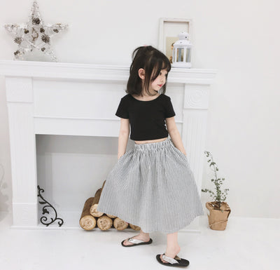 Young girl wearing a black short-sleeve crop top and a grey and white striped midi skirt with flip-flops. - Image 6