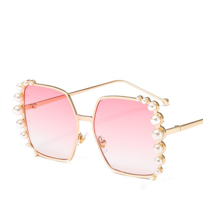 Oversized hexagonal sunglasses with gold-tone metallic frames, light pink lenses, and faux pearl embellishments.