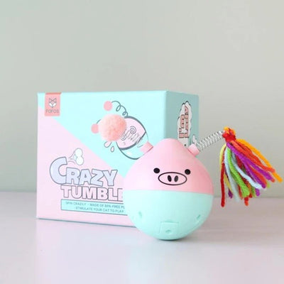 Pink and mint green pig-shaped tumbler pet toy with a colorful yarn tassel and spring, shown with its box.