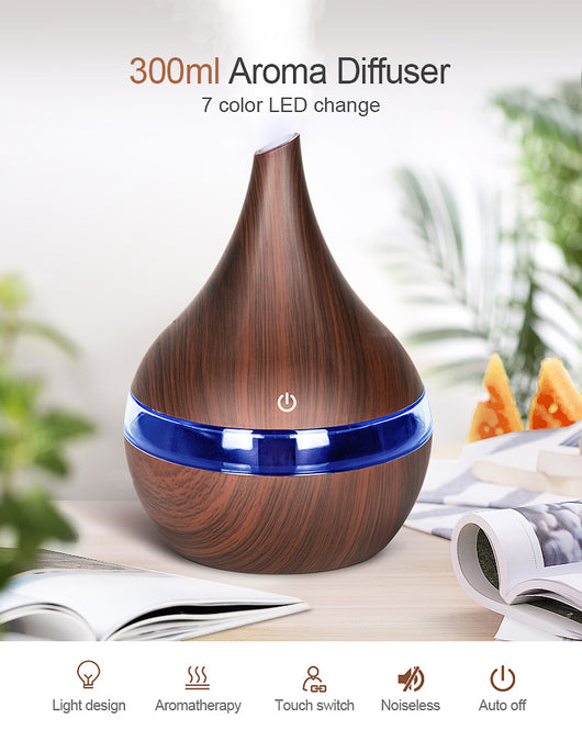 Dark wood grain LED essential oil diffuser with a blue light band and touch switch, shown with a hand operating it. Includes a bundle of 10 white filter sticks. - Image 5