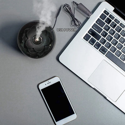 Black spherical aromatherapy humidifier with a lotus flower top, emitting mist, sitting on a gold decorative doily. - Image 12