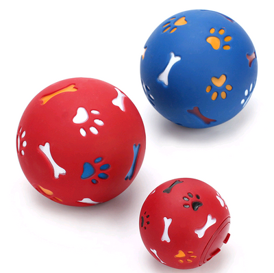 Red rubber pet puzzle ball with white, blue, and orange paw print and bone cutouts, featuring a treat dispenser opening. - Image 4